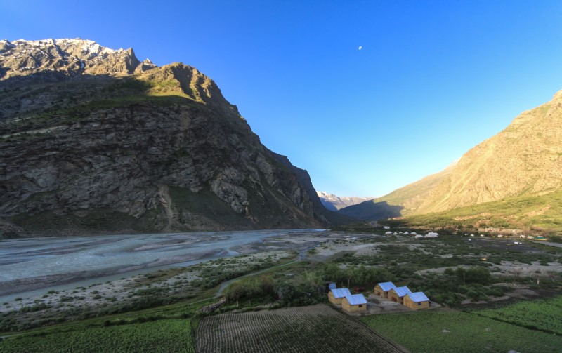 A landscape scene from India, with a mountain, blue sky, and small group of buildings.