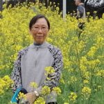 Angela Tsun sitting in a field of tall yellow flowers