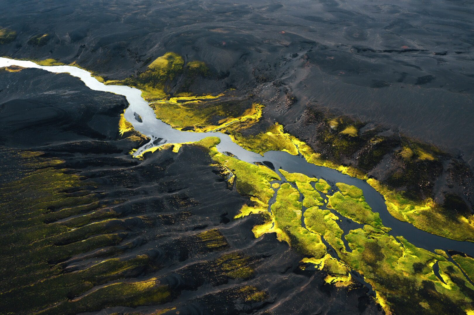 River seen from above, winding through a valley. Some parts are in the shade, with the sun illuminating other parts in a way that makes the water shine silver