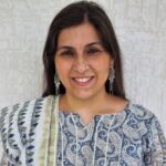 Jonaki Arora. Smiling woman with dark long hair wearing a sari and long silver earrings.