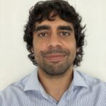 Kynan Barnes. Man with dark hair and a blue shirt smiles at camera