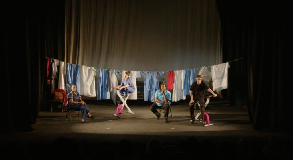 Four actors on a dark stage in various poses in front of a line of laundry