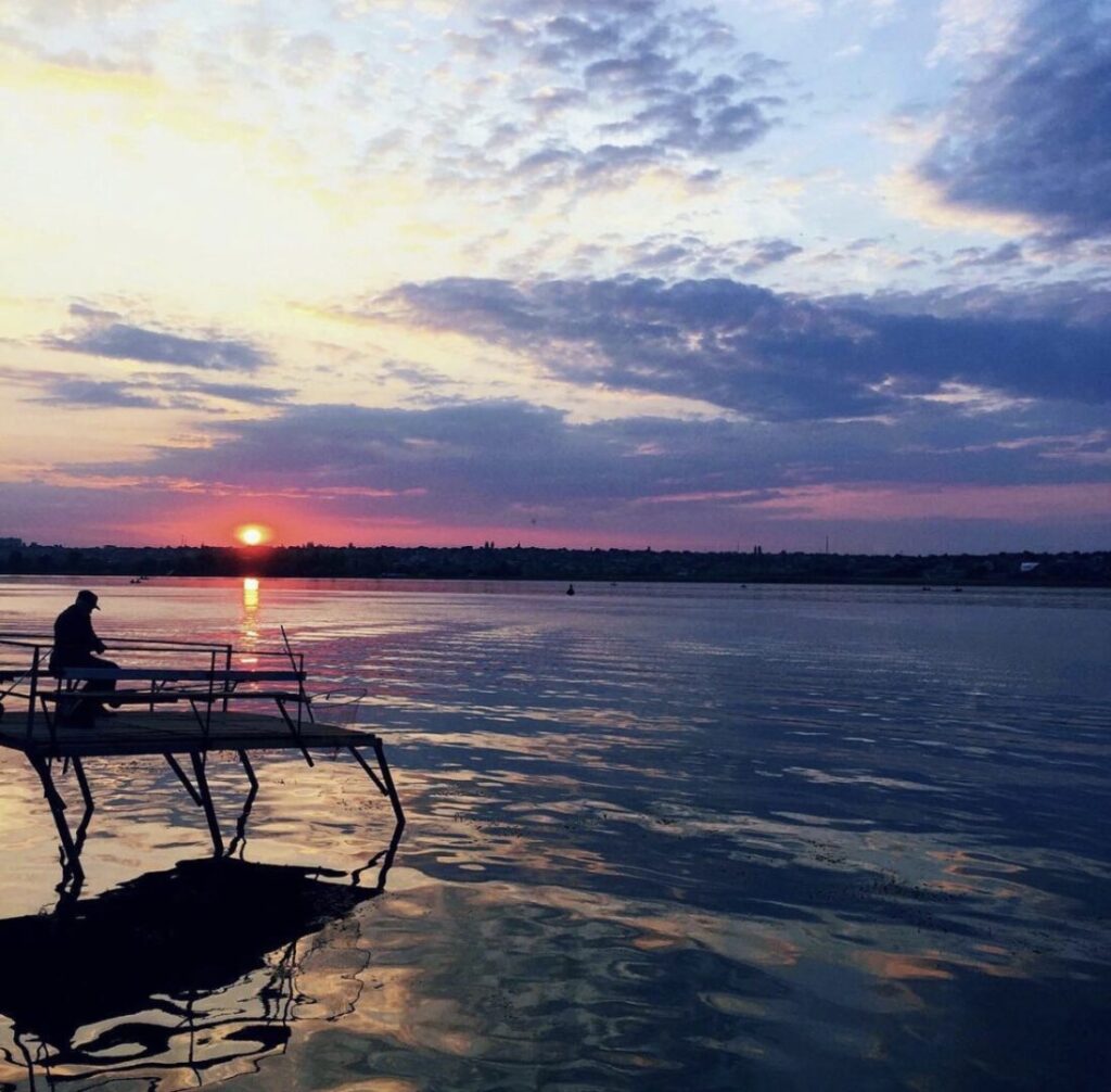 Silhouette of a person sitting on a bench the pier at sunset