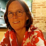Woman with shoulder length brown hair and glasses, wearing a red and white silk floral top