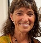 Woman with brown hair, light earrings and a beaded necklace