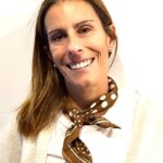 woman with long brown hair wearing a white shirt and cardigan, with a brown polkadot neckerchief