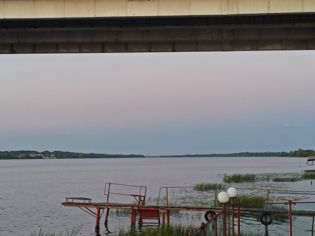 a wooden pier on a river in the evening light, with a variegated sky of dusky blue and pink in the horizon